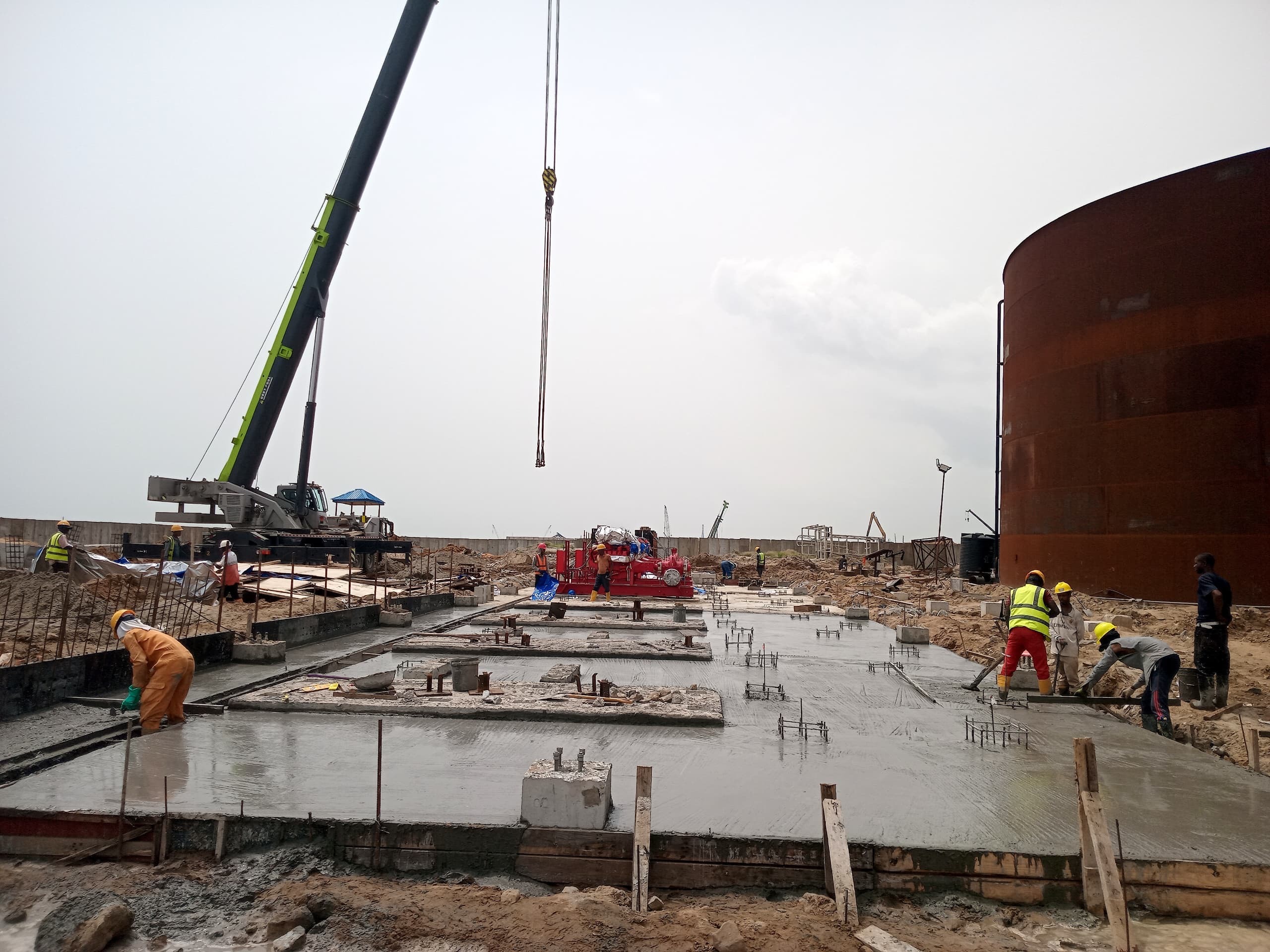 Steel framework of a partially constructed building on a construction site, surrounded by covered materials and equipment under a cloudy sky.